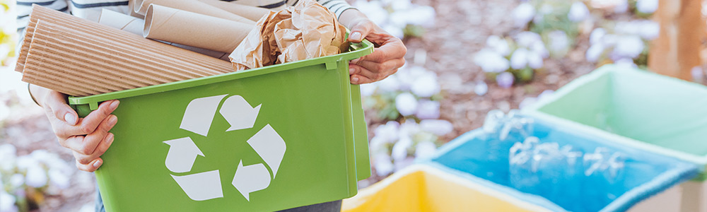 Woman holding a green recycling box containing cardboard paper and other recyclable materials